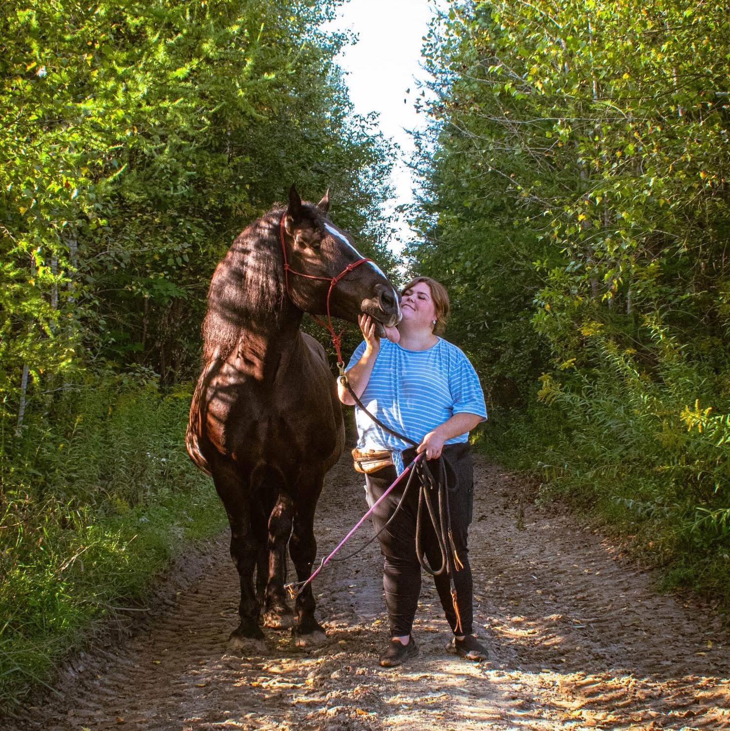 Bianca D. et son cheval Onyx, tête contre tête, sur un chemin en forêt